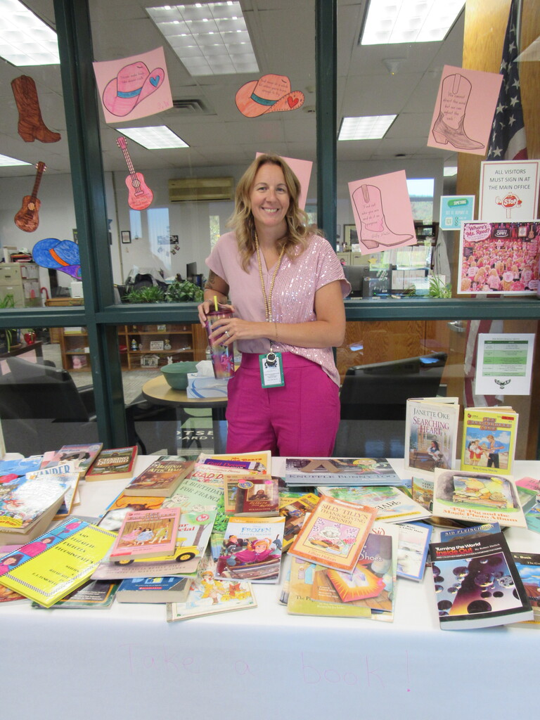 Staff member in pink posing in front of a table of free books for students