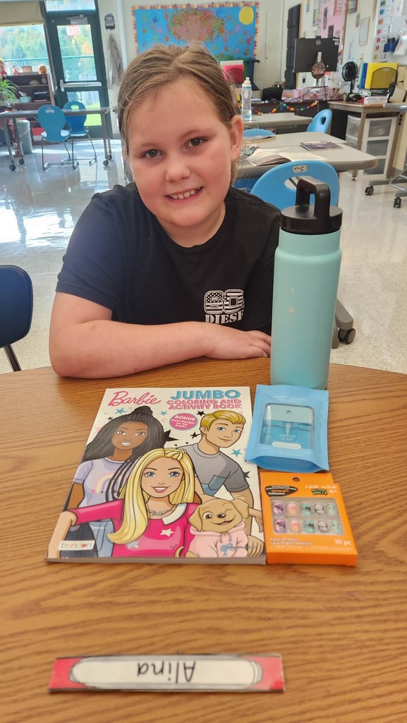 A student sitting at a desk with items from the auction including a water bottle and a Barbie coloring and activity book