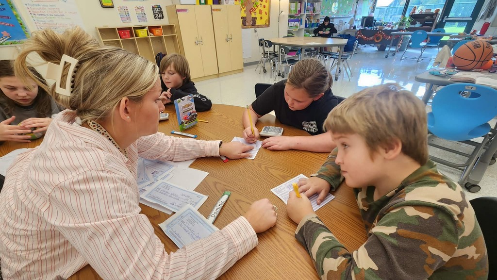 4 students sitting at a table and the teacher helping them write in their check registers
