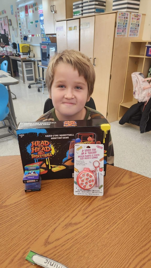 A student sitting at a table with items from the auction that include a Head to Head basketball game.