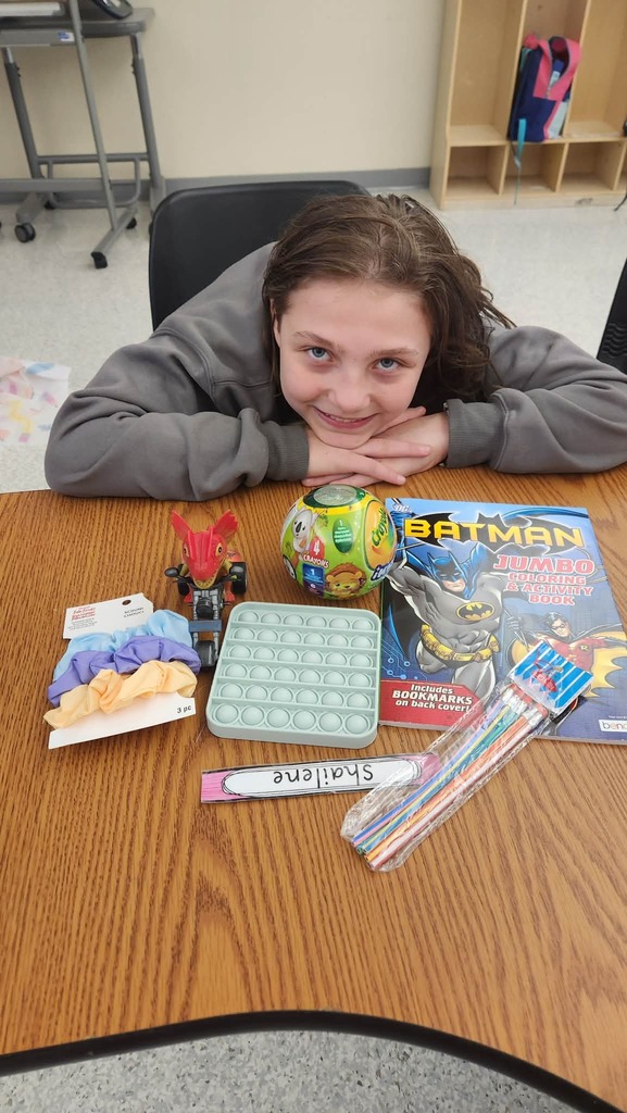 A student sitting at a table with their auction winnings that include hair accessories, a batman coloring book, and a fidget toy.