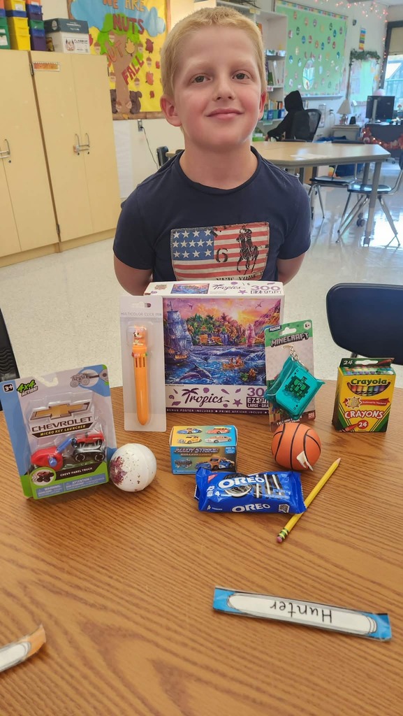 A student standing behind a table with items from the auction including a puzzle, a small package of Oreos and a box of crayons.