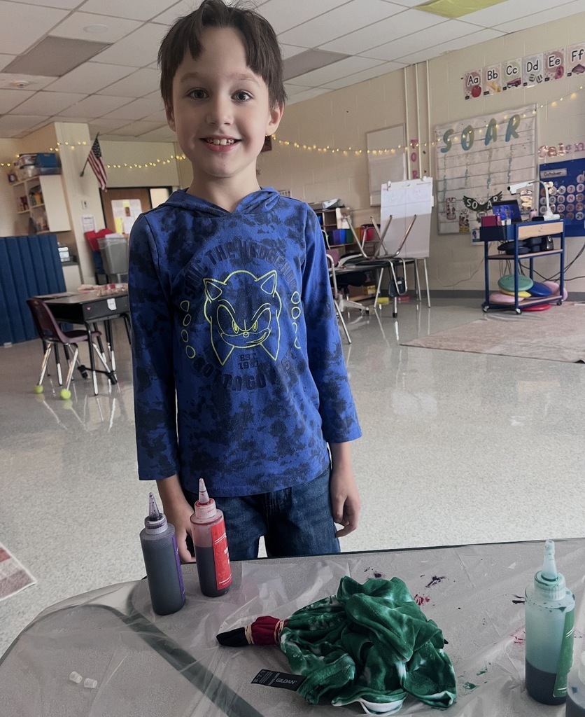 A student standing behind a table with two bottles of paint