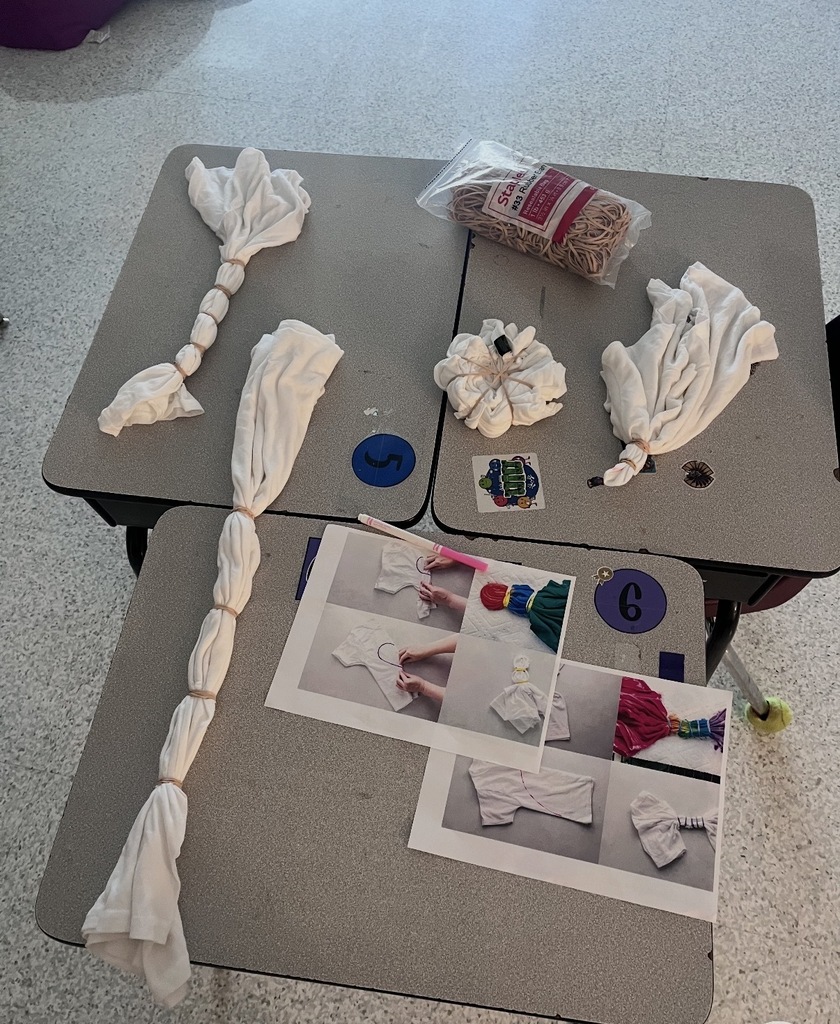 Shirts tied in rubberbands, printed instructions, and a bag of rubberbands on desks.