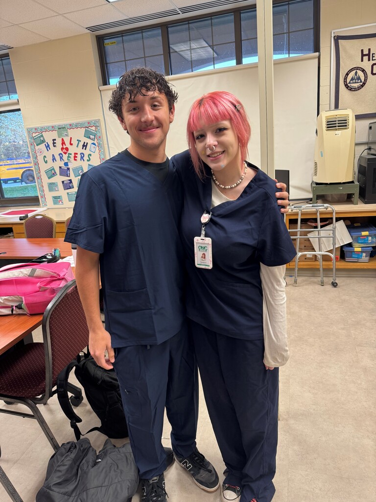Two students in blue medical scrubs posing for a picture in a classroom/