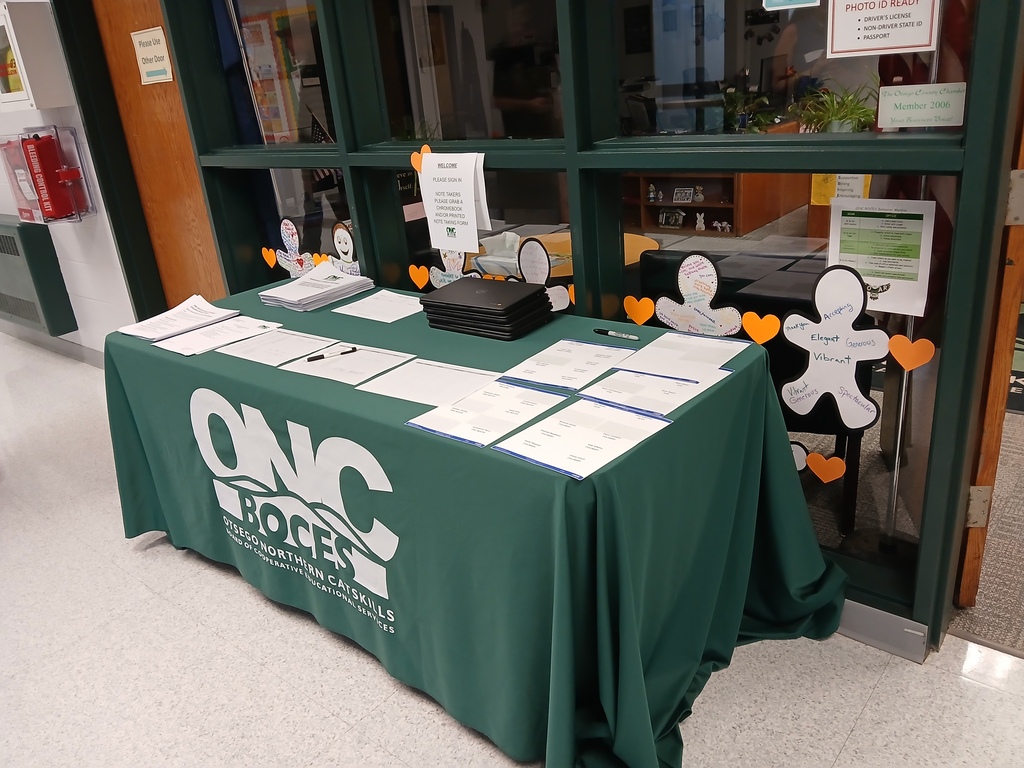 A table in the hallway with a green and white ONC BOCES tablecloth. There are papers, nametags, and pens on the table.