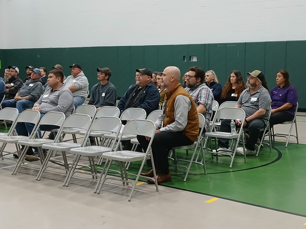 A picture of guests sitting in chairs in the gymnasium listening to the presenters.