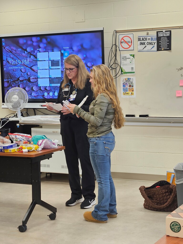 One student and the guest speaker standing in the front of the room looking at a medical breathing device.