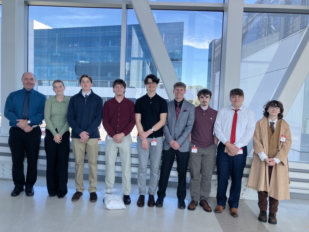 8 students and instructor standing in a hallway posing for a picture