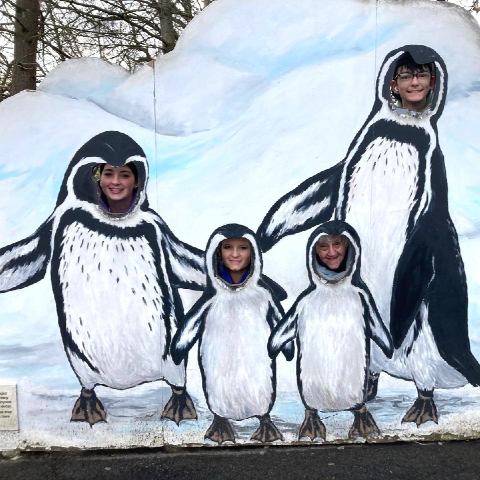 3 students and staff member posing in penguin cutout.