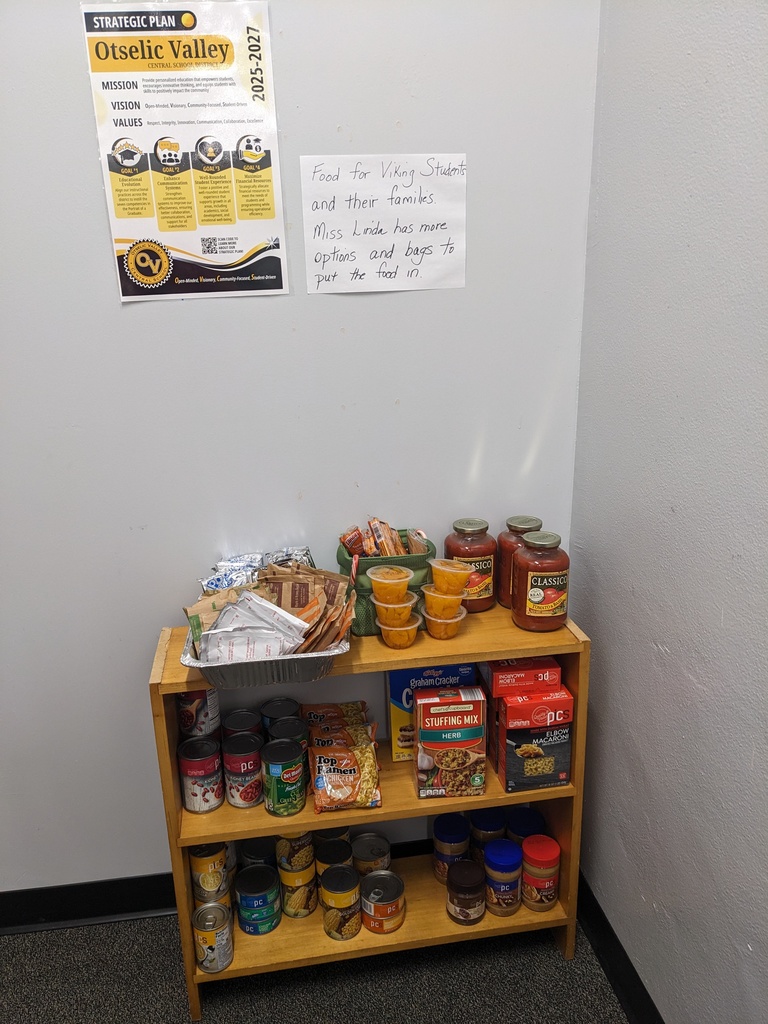 Small wooden shelf stocked with canned goods, pasta, peanut butter, snacks, and pasta sauce, with a sign above it noting food is available for Viking students and families.