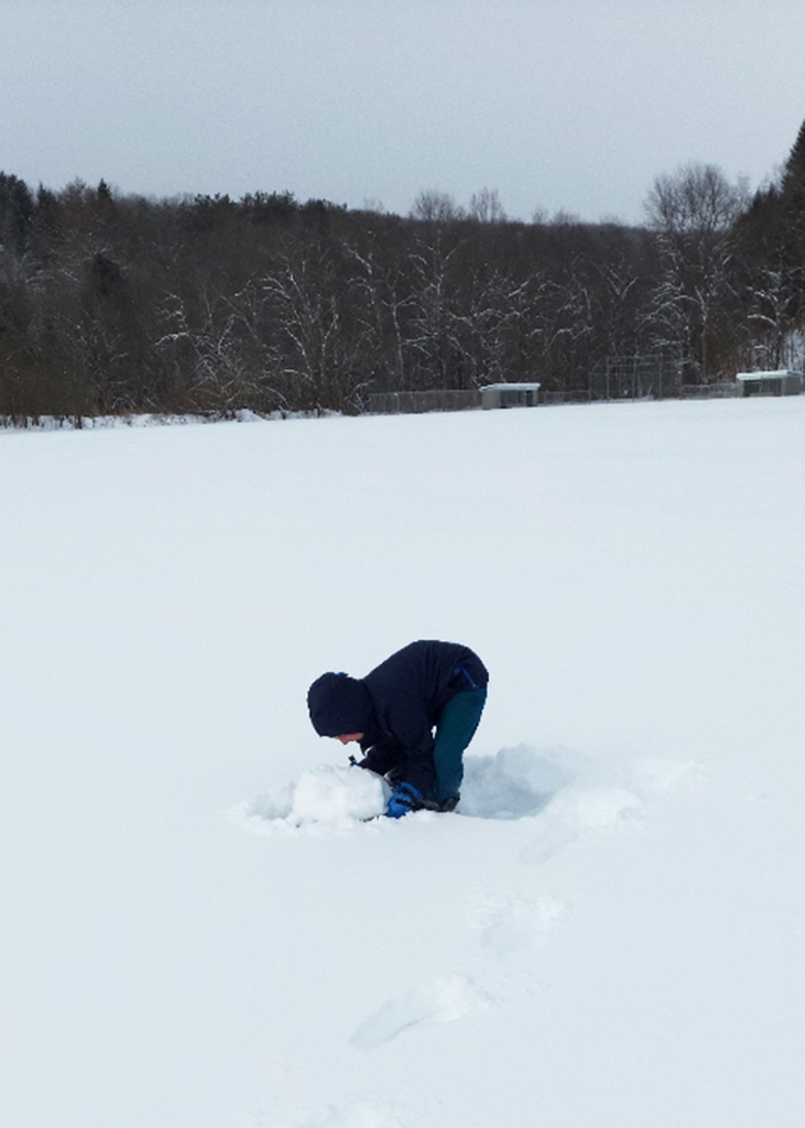 A student scooping up snow in a big bowl 