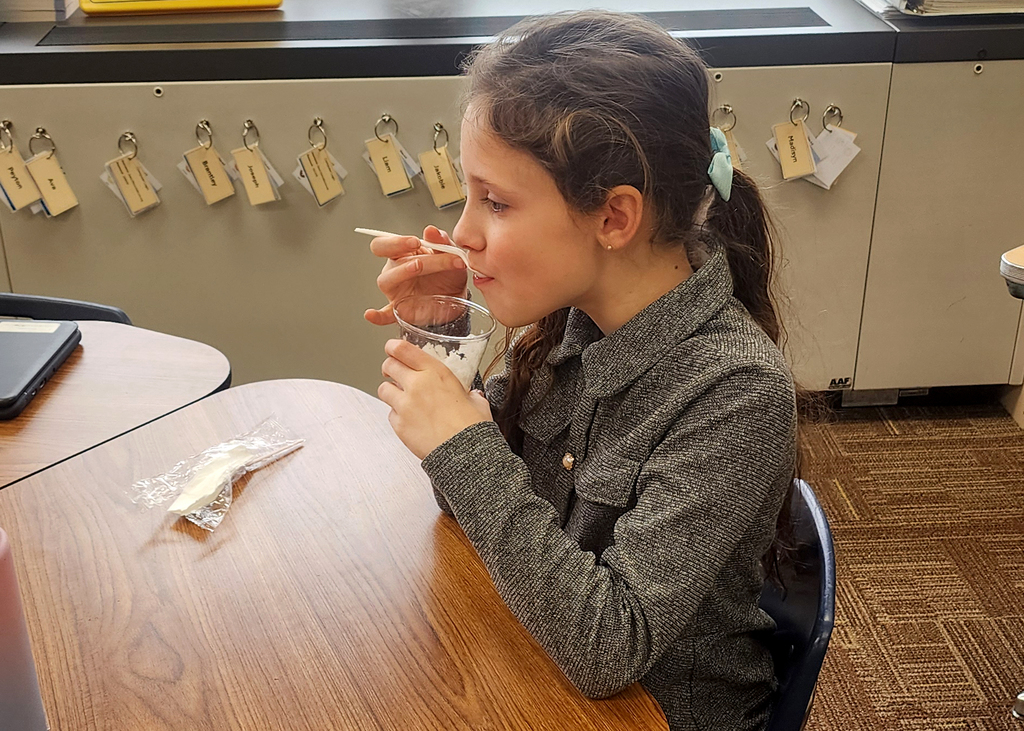 A student sitting at a desk eating snow ice cream