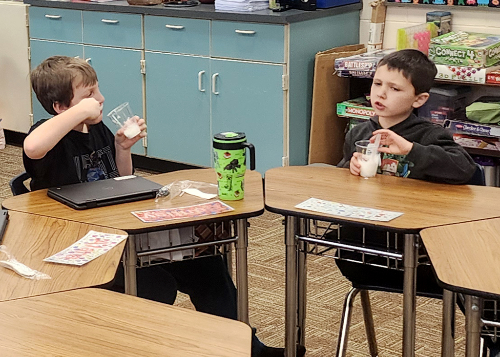 Classmates sitting at desks enjoying the snow ice cream