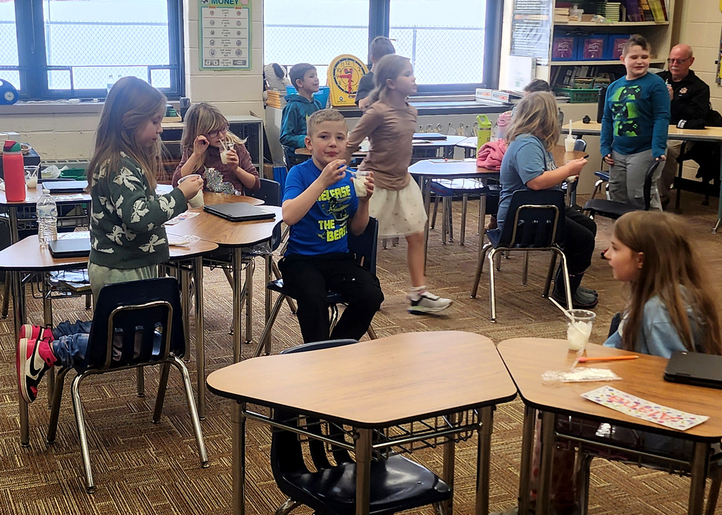 Classmates sitting at desks enjoying the snow ice cream
