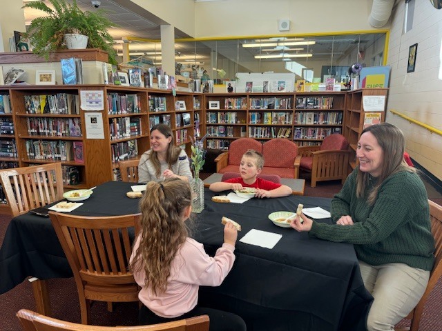 Students and teachers sit around the table eating soup and bread
