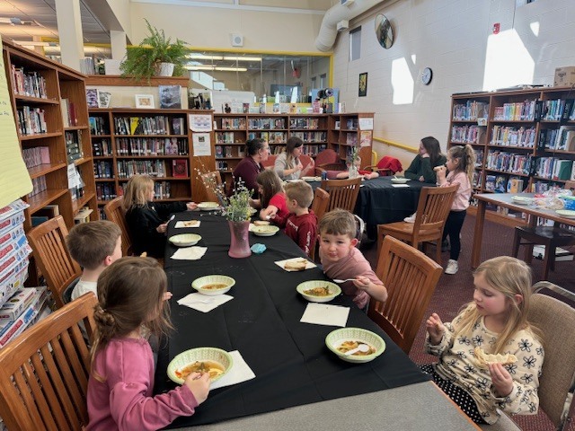 A wide shot of the class sitting at tables trying the soup