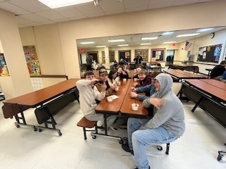 Group of students seated at a cafeteria table eating ice cream and smiling during the incentive celebration.