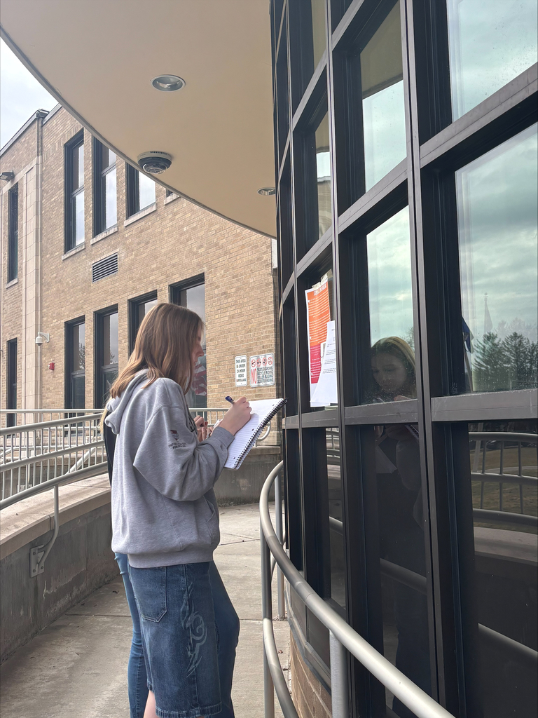 Student writing notes while standing outside near the school building during class.
