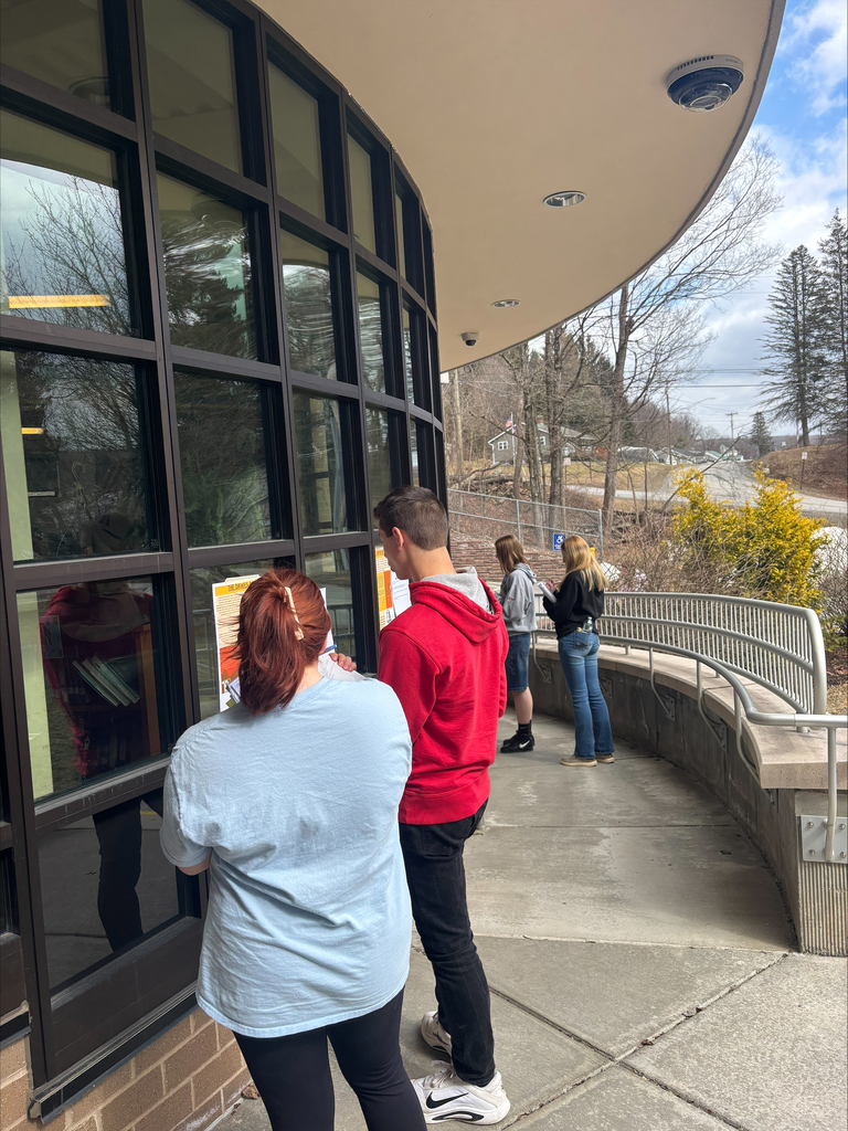 Students standing outside the school building taking notes during a class activity.