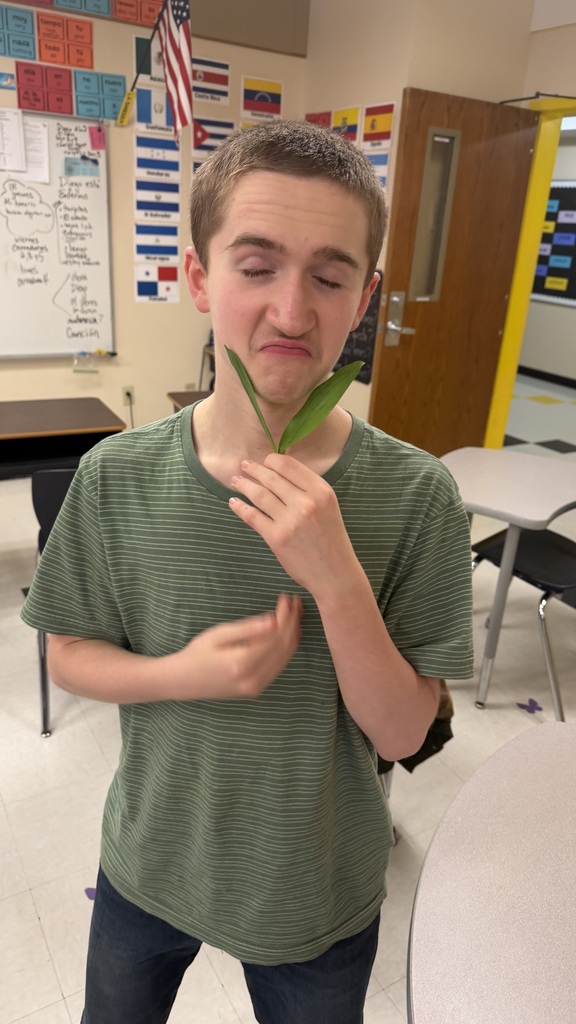 Student holds ramp leaves in classroom with playful expression during cooking lesson.