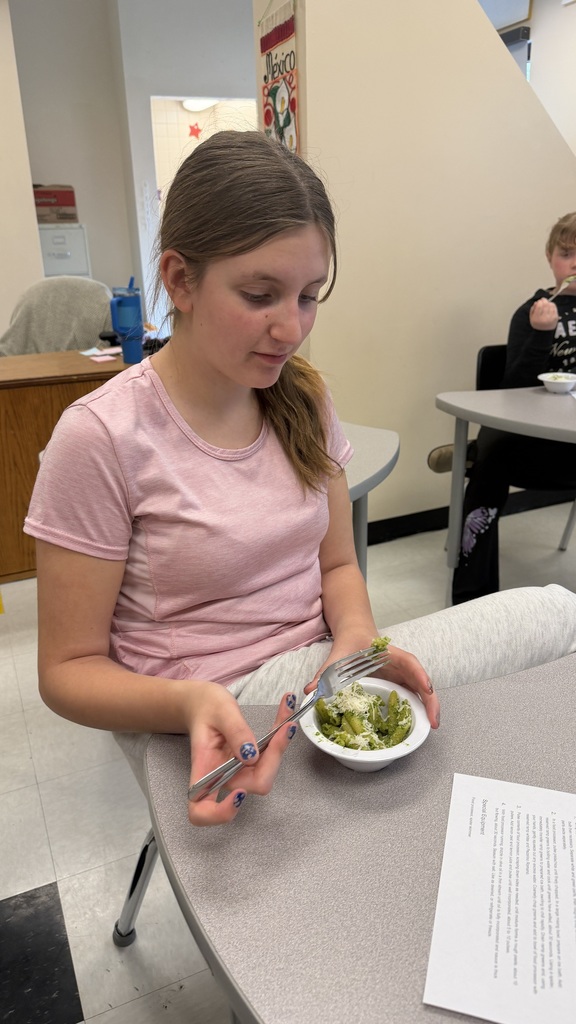Student sits at table eating bowl of ramp pesto pasta.