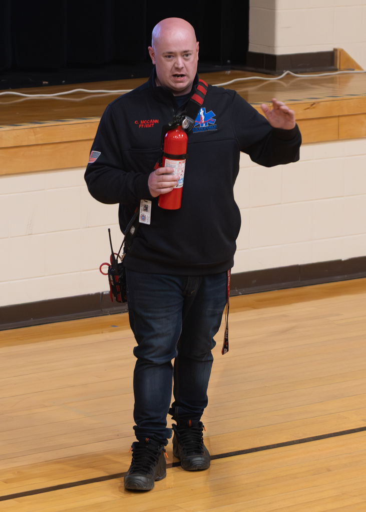 Staff member talks about using  a fire extinguisher while speaking to students in the auditorium.
