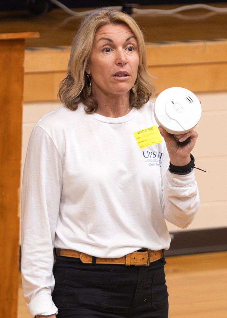 Guest presenter displays a smoke detector while speaking about home fire prevention and alarm safety.