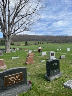 Students work throughout a cemetery, picking up debris among headstones on a grassy hillside.