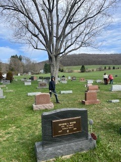 Students work throughout a cemetery, picking up debris among headstones on a grassy hillside.