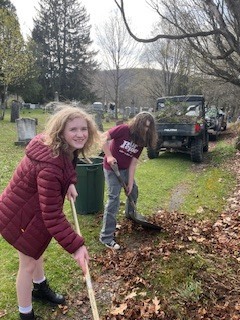 Two students rake leaves near a path, smiling while working during the clean-up.