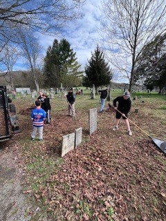 Students rake leaves and clear debris around gravestones during a cemetery clean-up.