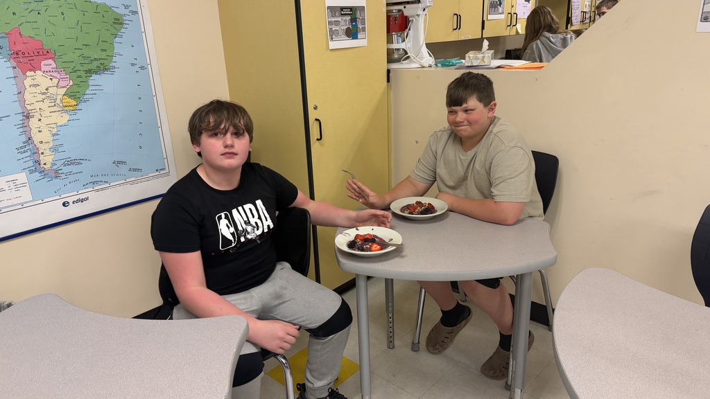 Students in a classroom preparing açaí bowls with fresh fruit and toppings during a cooking lesson.