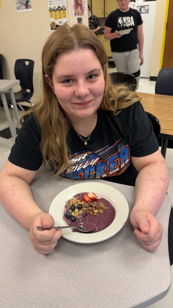 Students in a classroom preparing açaí bowls with fresh fruit and toppings during a cooking lesson.