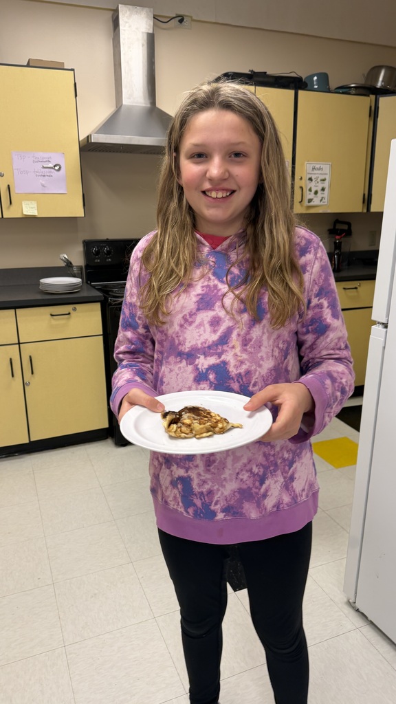 Sixth grade students prepare pancakes in a classroom cooking activity with help from classmates