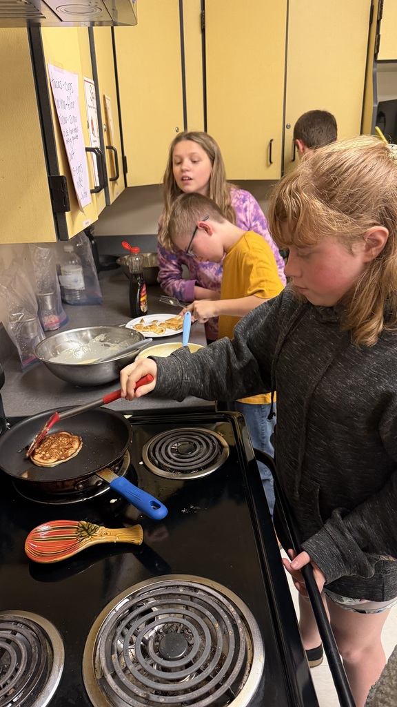 Sixth grade students prepare pancakes in a classroom cooking activity with help from classmates