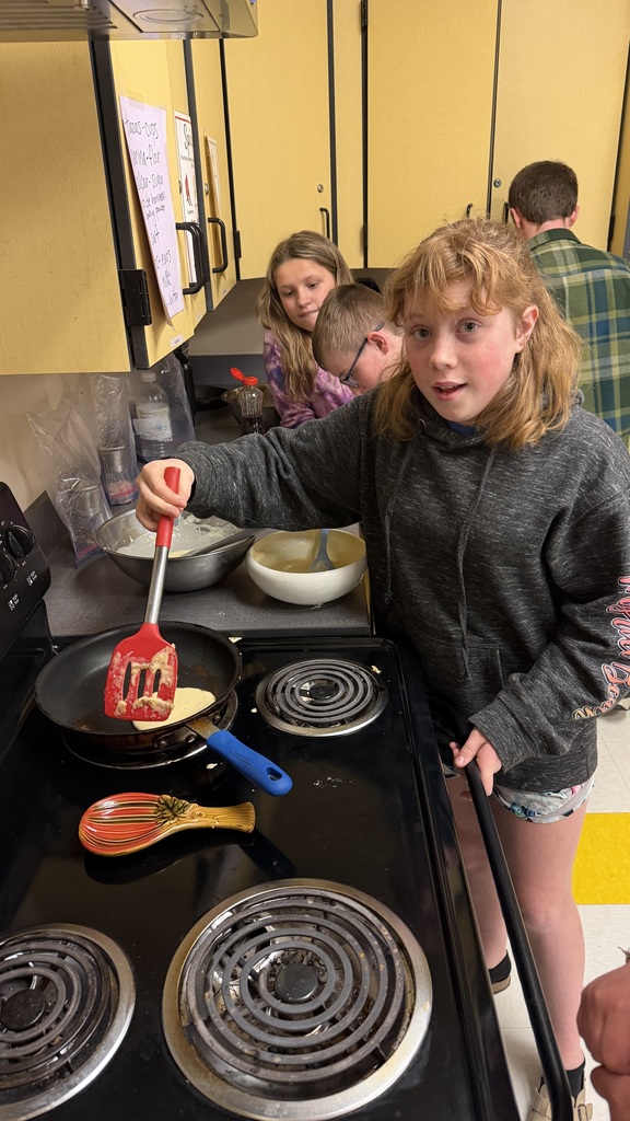 Sixth grade students prepare pancakes in a classroom cooking activity with help from classmates