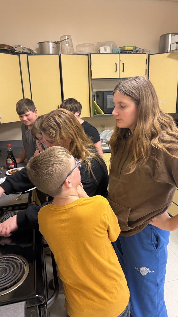 Sixth grade students prepare pancakes in a classroom cooking activity with help from classmates