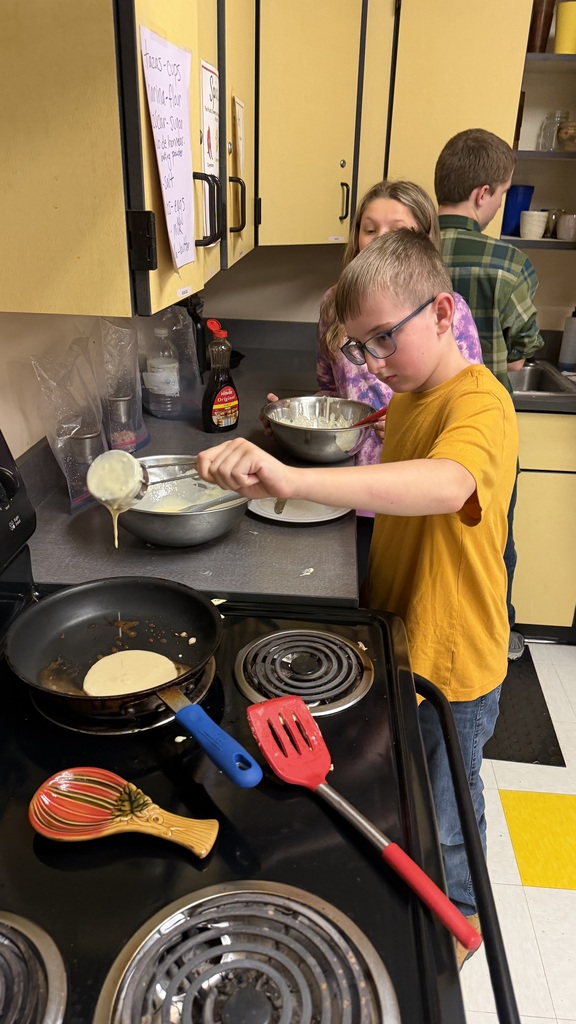 Sixth grade students prepare pancakes in a classroom cooking activity with help from classmates