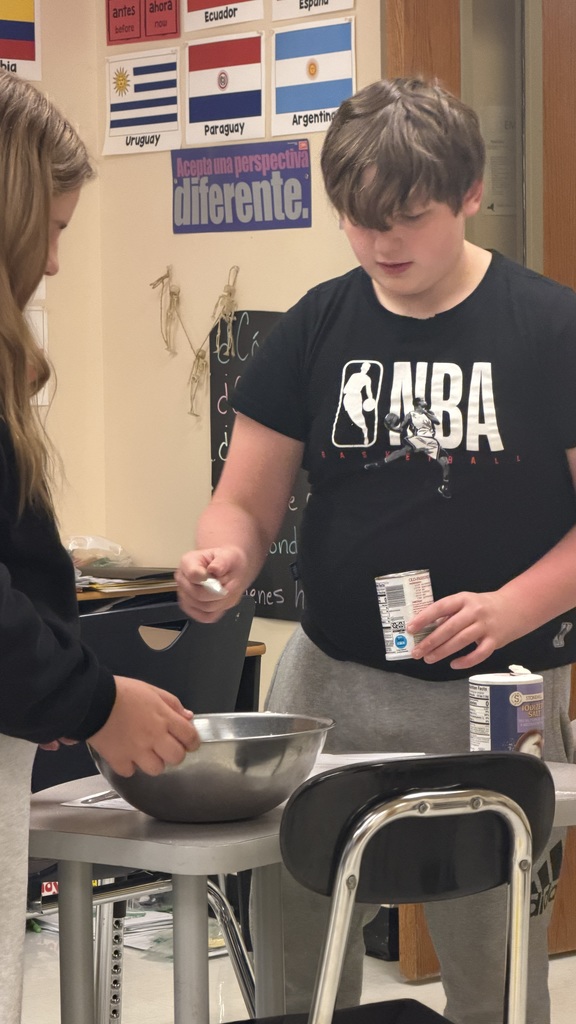 Sixth grade students prepare pancakes in a classroom cooking activity with help from classmates