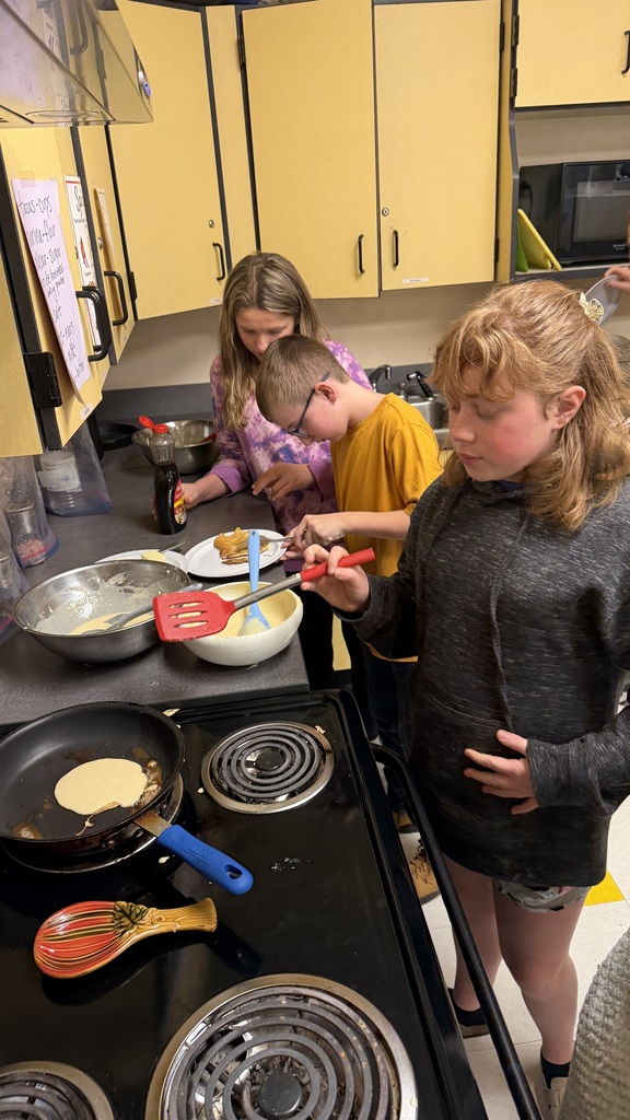 Sixth grade students prepare pancakes in a classroom cooking activity with help from classmates