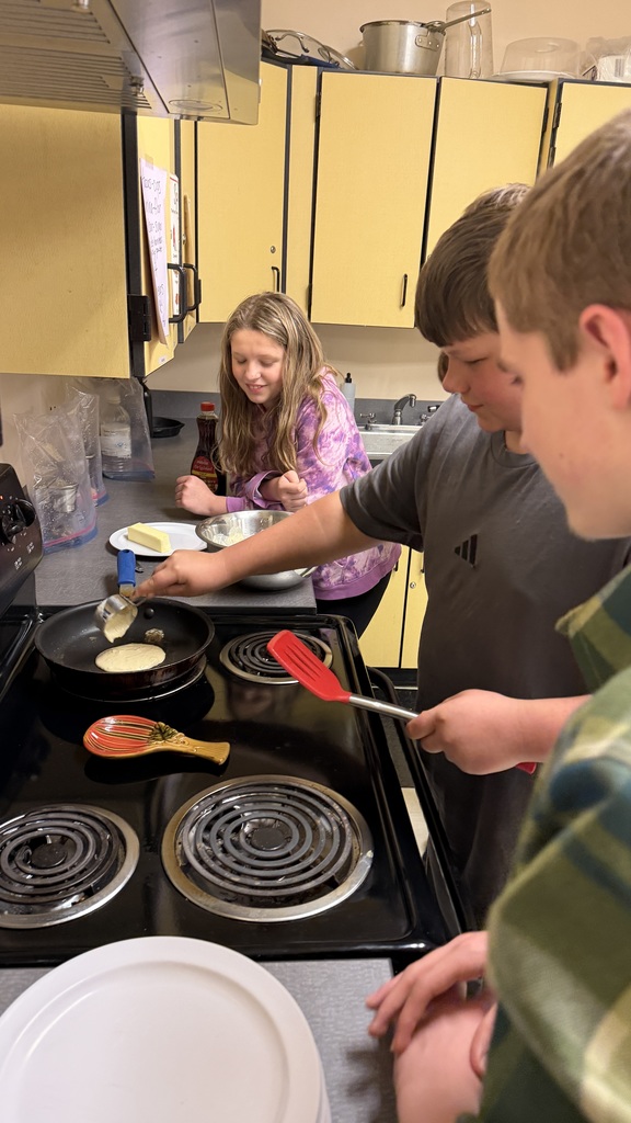 Sixth grade students prepare pancakes in a classroom cooking activity with help from classmates
