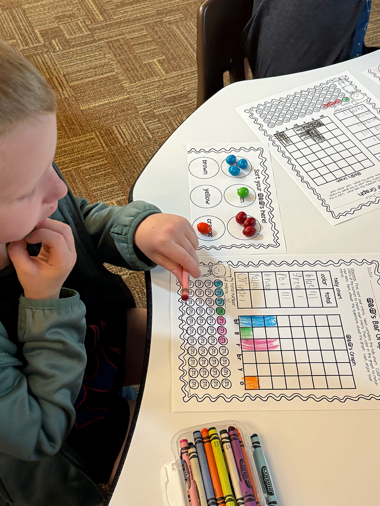First grade students participate in a hands-on math activity using M&Ms to practice sorting, tally charts, and graphing skills in the classroom.