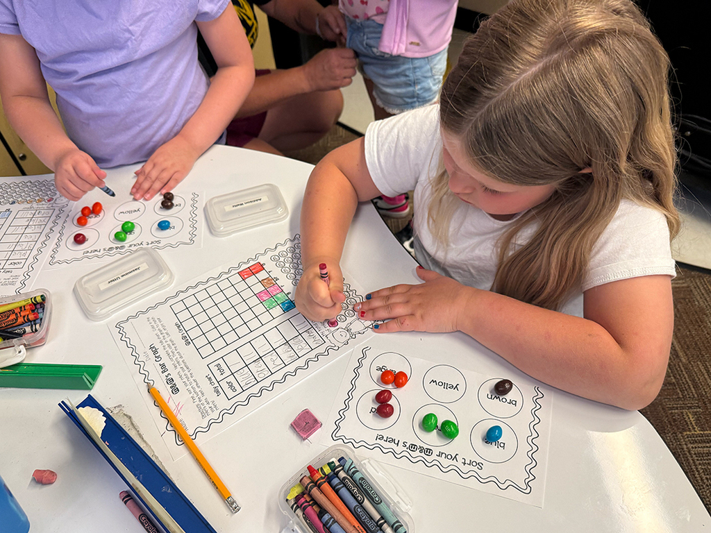 First grade students participate in a hands-on math activity using M&Ms to practice sorting, tally charts, and graphing skills in the classroom.