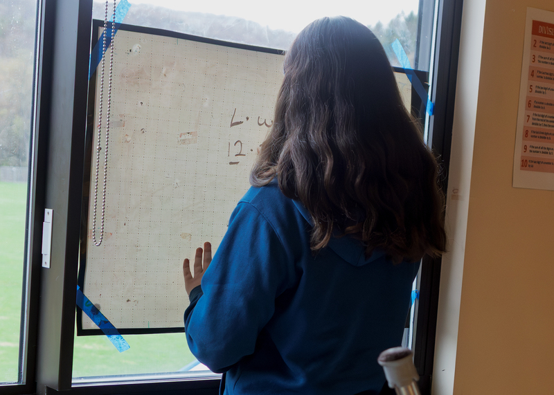 Student works on a math problem using a window-mounted whiteboard during class.