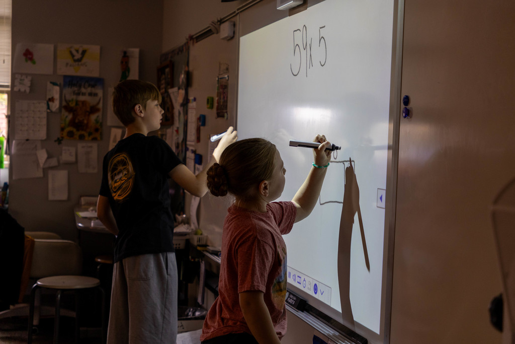 Kids doing math problem on white board.