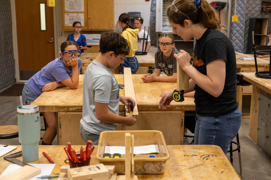 Wood Shop teacher at Ottawa Middle School helping a student use a tape measurer.
