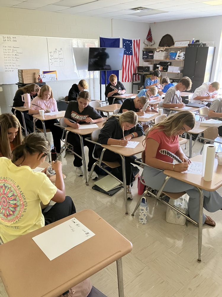 8th grade students practice writing name with feather pens