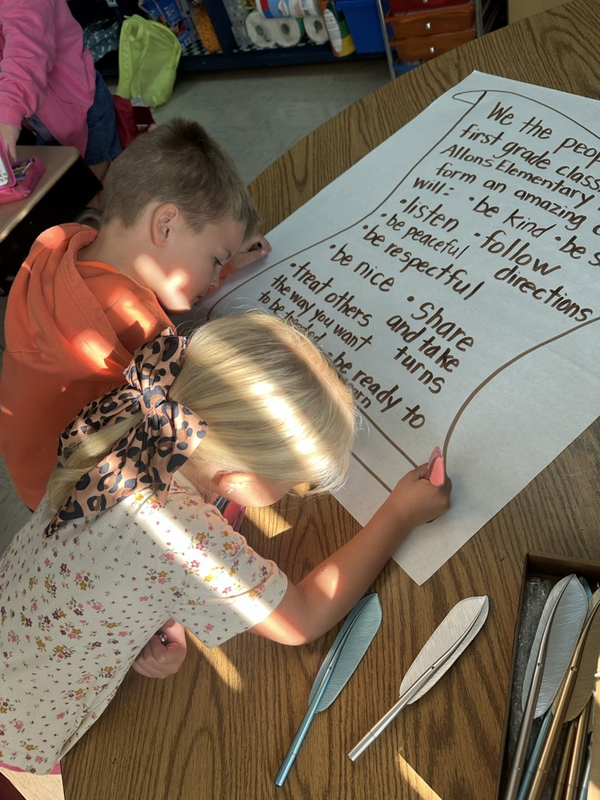first grade students signing their classroom constitution with feather pens