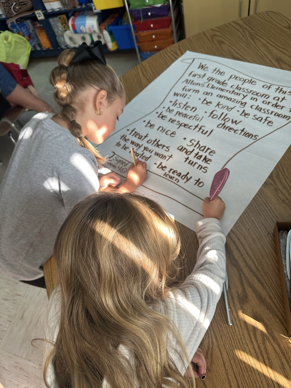 first grade students signing their classroom constitution with feather pens